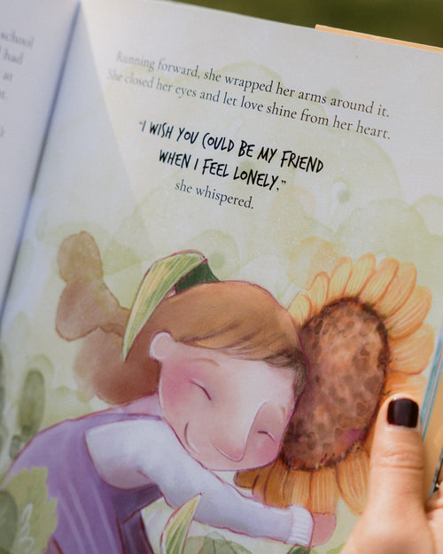 Illustrated book page with a girl hugging a sunflower and text, held by a hand.